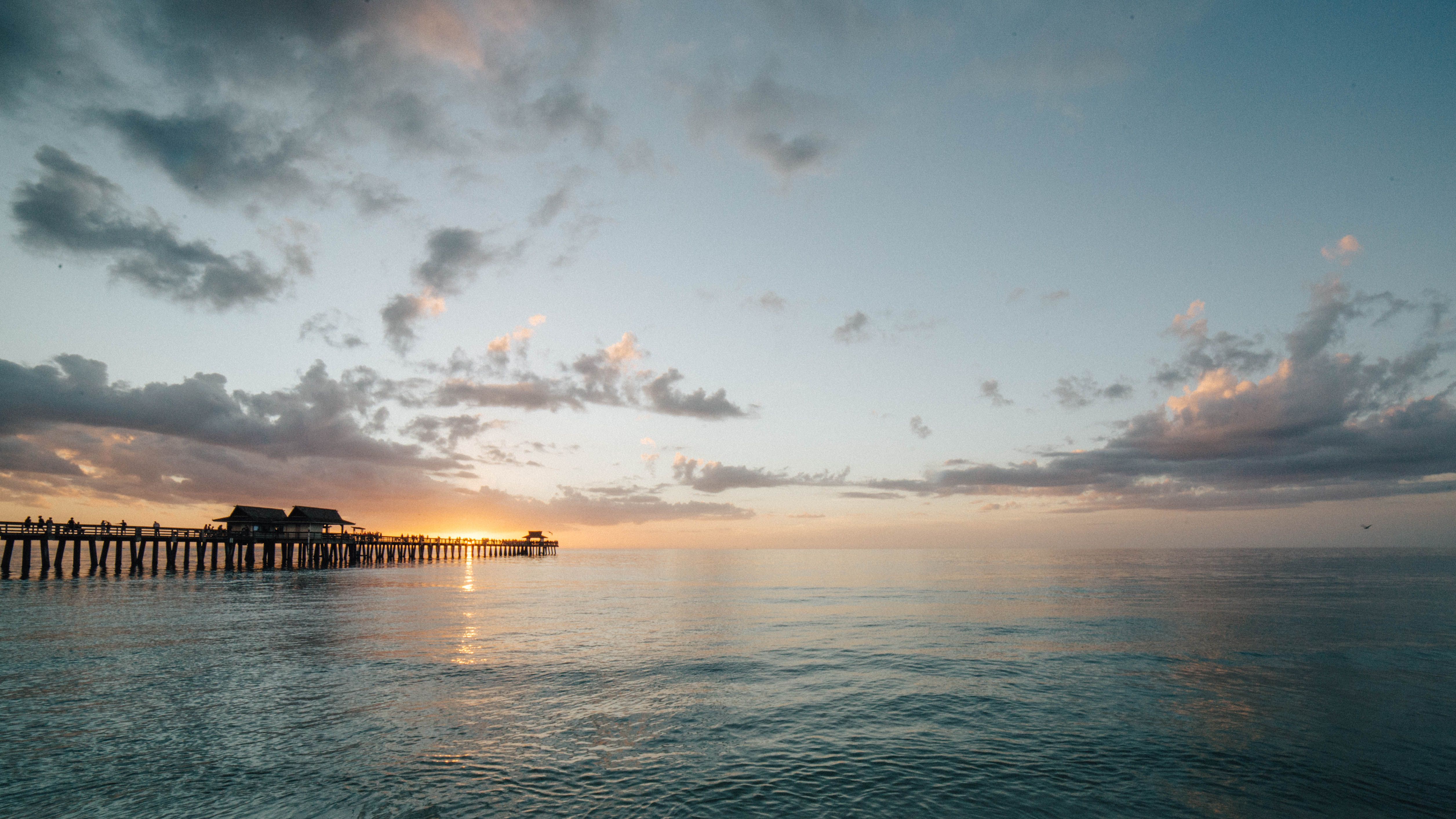 The Naples Pier silhouetted against a golden sunset over the Gulf